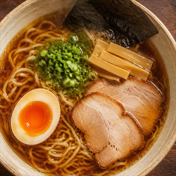 湯気が立つ醤油ラーメン。半熟卵、チャーシュー、ねぎ、メンマ、海苔が盛り付けられている